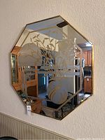 Front view of octagonal mirror showing the etched floral design with a vase and gold frame on a light wall.