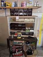 Full view of shelves and workbench showing multiple plastic bins filled with assorted hardware like screws, nails, washers, nuts, steel wool can, paper towel rolls, and a yellow portable radio.
