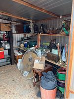 Photo showing inside shed with metal shelving, large round mirror, wooden table, candlestick holders, and various decor items.