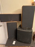 Four speakers stacked in corner: two Boston rectangular speakers with black grilles and wood sides, one Klipsch large center channel speaker with wood veneer and Klipsch badge, and a Klipsch subwoofer with black grille.