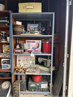 Full view of steel shelving cabinet with items on four shelves showing items like toolbox, power tool, massage product, red container, sewing machine, vintage electronics.