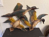 Set of three metal duck sculptures mounted on wall and placed on table.