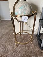 Full frontal view of the globe on tall brass stand showing the entire setup from the front with carpeted flooring.