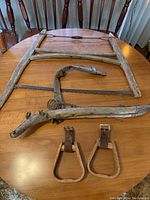 Photo of large wooden tree crosscut saw, wood animal harness, and wooden stirrups on wooden table