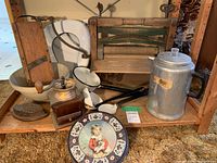 Wooden wringer washer, metal percolator, vintage iron, enamelware, wooden slicer, and decorative plate arranged on wooden floor