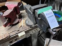 Two heavy duty bench vises on workbench. One black with 3-inch jaws and one red Wilton Scout 4-inch jaw model.