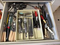 First drawer with various stainless steel cutlery including spoons, forks, knives, plus can opener and cutting tools