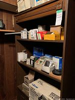 Shelving with assortment of electrical items including boxes of outlets, door chimes, and fan parts