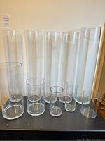Seven clear, cylindrical glass vases arranged by height on a flat surface, showing the full set.