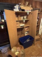 Overall view showing wooden cabinet with various light fixtures and shades stored inside. Box on floor contains glass light shades and lighting parts.