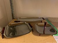 Three chrome serving trays with red Bakelite handles and feet shown together on a shelf.