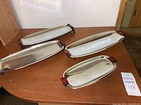 All four mid century footed serving trays displayed on a wooden surface, showing stainless steel body with red Bakelite handles.