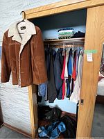 Wide shot of closet front showing brown corduroy sherpa jacket hanging and assortment of shirts, jackets, bags on floor