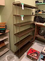 Full view of the metal shelf showing wood look shelves against a green wall, with some items around and a tag attached.
