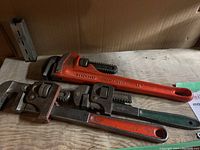Three Ridgid pipe wrenches of different sizes with red handles on a wooden surface.