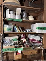 Wide shelf view showing multiple rolls of tape on upper shelves and boxes and assorted plumbing parts below, including Price Pfister boxed faucet
