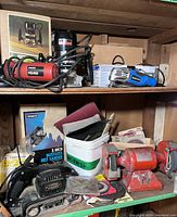 Shelf with various power tools including Hilti HG450 angle grinder, Craftsman router in box, sanding belts, and a red double wheel grinder/buffer.