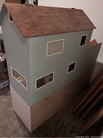 Side view of the wooden Barbie dollhouse showing painted walls, windows, and natural wood roof with removable base