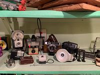Photo of assortment of vintage cameras and accessories including Brownie Starflash, Olympus camera, Canon camera and various flash units arranged on a green shelf