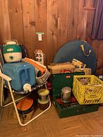 Overview of the collection of vintage camping gear including Coleman stoves, water jug, camping chair, tarps, tent, yellow crate with miscellaneous items
