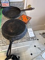 Two cast iron frying pans, one with wooden handle and one with cast iron handle, shown from top and side views on countertop.