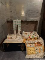 Photo of various vintage baby linens including Winnie the Pooh quilt, towels, and patchwork blanket inside a vintage trunk