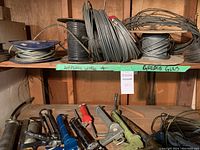 View of multiple spools and coils of airplane wire and cable on upper shelf with grease guns on lower shelf