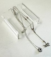 Two delicate silver necklaces displayed separately, showing rose and dog pendants respectively.