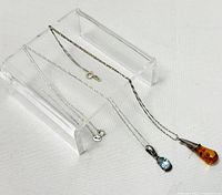 Two silver chain necklaces displayed side by side showing the full length and both pendants clearly visible.