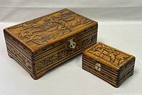 Two carved wooden jewelry boxes side by side showing detailed exterior carvings and locking mechanisms.