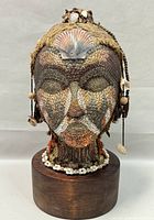 Front view of the handcrafted bust sculpture showing detailed texture and facial paint markings, along with a large shell on the forehead and smaller shells and beads on sides.