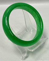 Front view of a polished green jade bangle bracelet displayed on a clear stand.