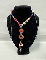 Front view of necklace displayed on black velvet bust showing coral beads, blue and white stones, and brown circular bead with coral center and dangling bead section.