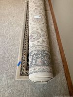 Photo showing the rolled-up oriental style area rug on a carpeted floor, displaying the beige and floral pattern on the front side.