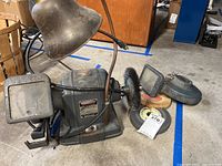 Full view of the Craftsman bench grinder showing metal body, two grinding wheels, wire brush wheel, and extra stone along with a lamp.