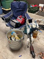Items shown in garage environment: blue folding chair holding two cooler bags, aluminum trash can with bird seed bags, brown bottle, closed umbrella with wooden handle, and other miscellaneous items around.