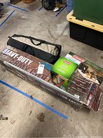 Two boxed heavy-duty army cots with carry bag tent and Coleman coffee pot on concrete floor.