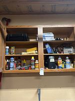 Wooden wall cabinet with assorted car care products, sprays, and tools displayed on two shelves.