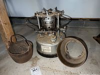 Full lot showing metal burner with coil, separate rusted fire pot with handle, and rusty circular metal part