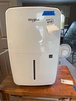 Front view of the white Whirlpool dehumidifier with blue tape showing date and a Maxsold sticker on the front.