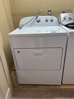 Front view of white Whirlpool electric dryer with closed door and visible power cord.
