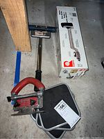 Photo showing the Roberts knee kicker with red handle, sliding pads, and carpet trimmer box laid on the floor.