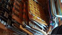 Seven colorful outdoor folding chairs stacked and leaning inside a shed, visible metal frames and woven fabric seats.