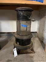 Full view of the Perfection oil heater showing metal base, glass cylinder with crack and rusted perforated metal top support.