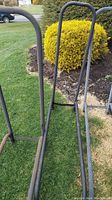 Full view of metal double log holder on grass with yellow bushes in background showing two U-shaped metal frames for logs.