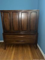 Full view of walnut chest showing two upper cabinet doors and two lower drawers against blue walls