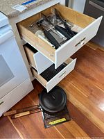 Open drawers showing kitchen utensils including peelers, whisks, grilling basket and Lodge cast iron lid on bottom shelf