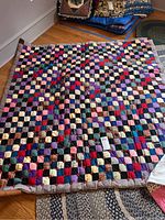 Multicolored patchwork quilt spread on floor, showing overall checkered pattern and colors.