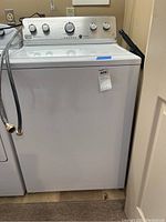 Front view of the white Maytag washing machine with hoses attached and a MaxSold price tag.