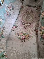 Partially rolled rug showing floral medallion and rose bouquet on beige field